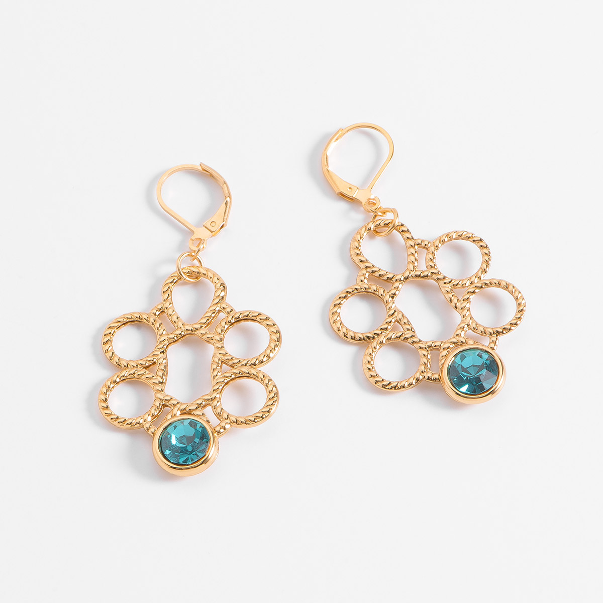 Aretes con un diseño geométrico compuesto por un patrón de círculos entrelazados, con un acabado texturizado. De la parte inferior de cada arete, se destaca una piedra en tono azul.
-        Aretes medianos
-        Patente
-        Baño de Oro 18k
-        Piedra en tono azul
