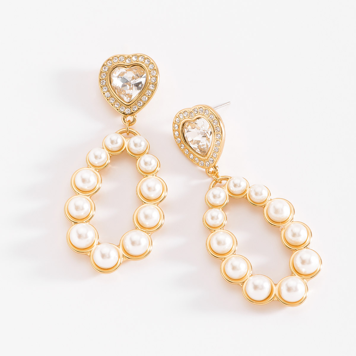 Aretes en baño de oro con un diseño espectacular. Cada arete comienza con una piedra en tono cristal en forma de corazón, incrustada con piedras en tono cristal. Debajo del corazón, una estructura ovalada está incrustada con perlas que la rodean. Combínalos con tu collar y pulsera.
-        Aretes largos
-        Poste
-        Baño de Oro 18k
-        Perlas en tono cream