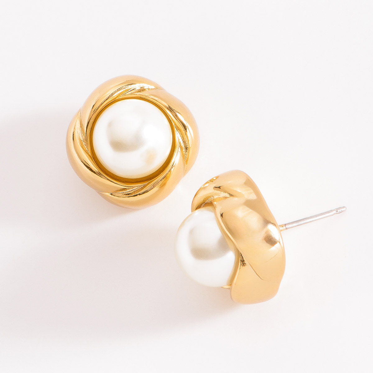 Aretes en baño de oro, cada uno con una perla en tono cream, envuelta en un diseño de nudo dorado.
-        Aretes chicos
-        Poste
-        Baño de Oro 18k
-        Perla en tono cream

