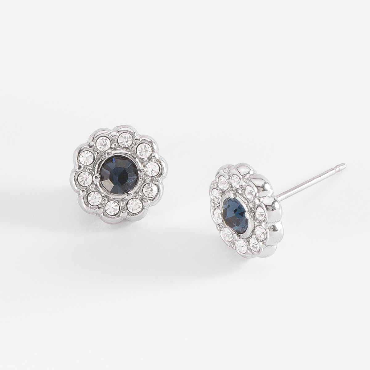 Aretes de botón con diseño floral en baño de platino. En el centro destaca una piedra en tono azul oscuro, y en cada pétalo una piedra en tono cristal. Combínalos con tu collar, pulsera y anillo.
-        Aretes chicos
-        Poste
-        Baño de Platino
-        Piedras en tono cristal y azul claro
