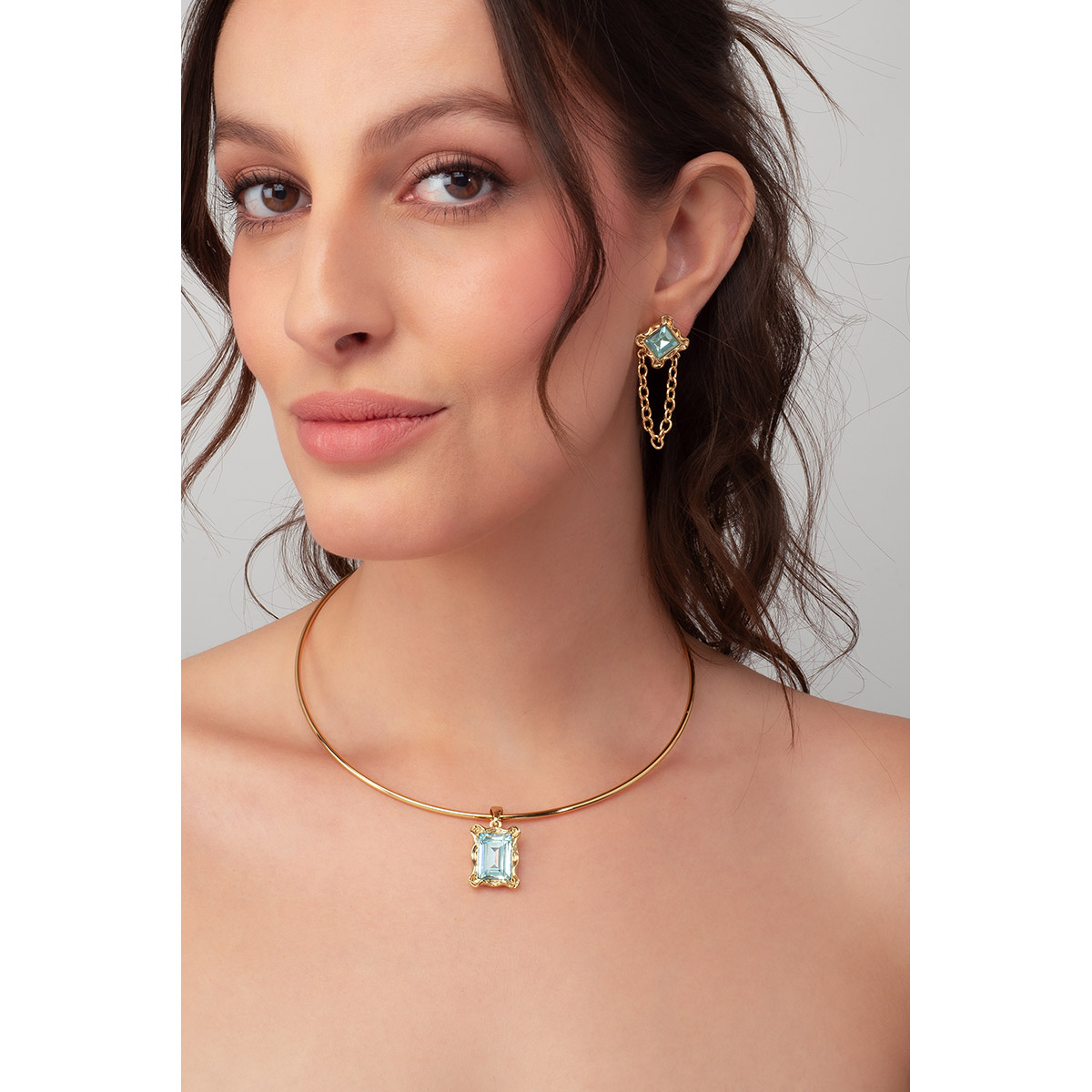 Aretes en baño de oro, incrustados con una piedra cuadrada en tono aguamarina, con una pequeña cadena de eslabones que cuelga del centro. Combínalos con tu collar y pulsera.
-        Aretes largos
-        Poste
-        Baño de Oro 18k
-        Piedra en tono aguamarina