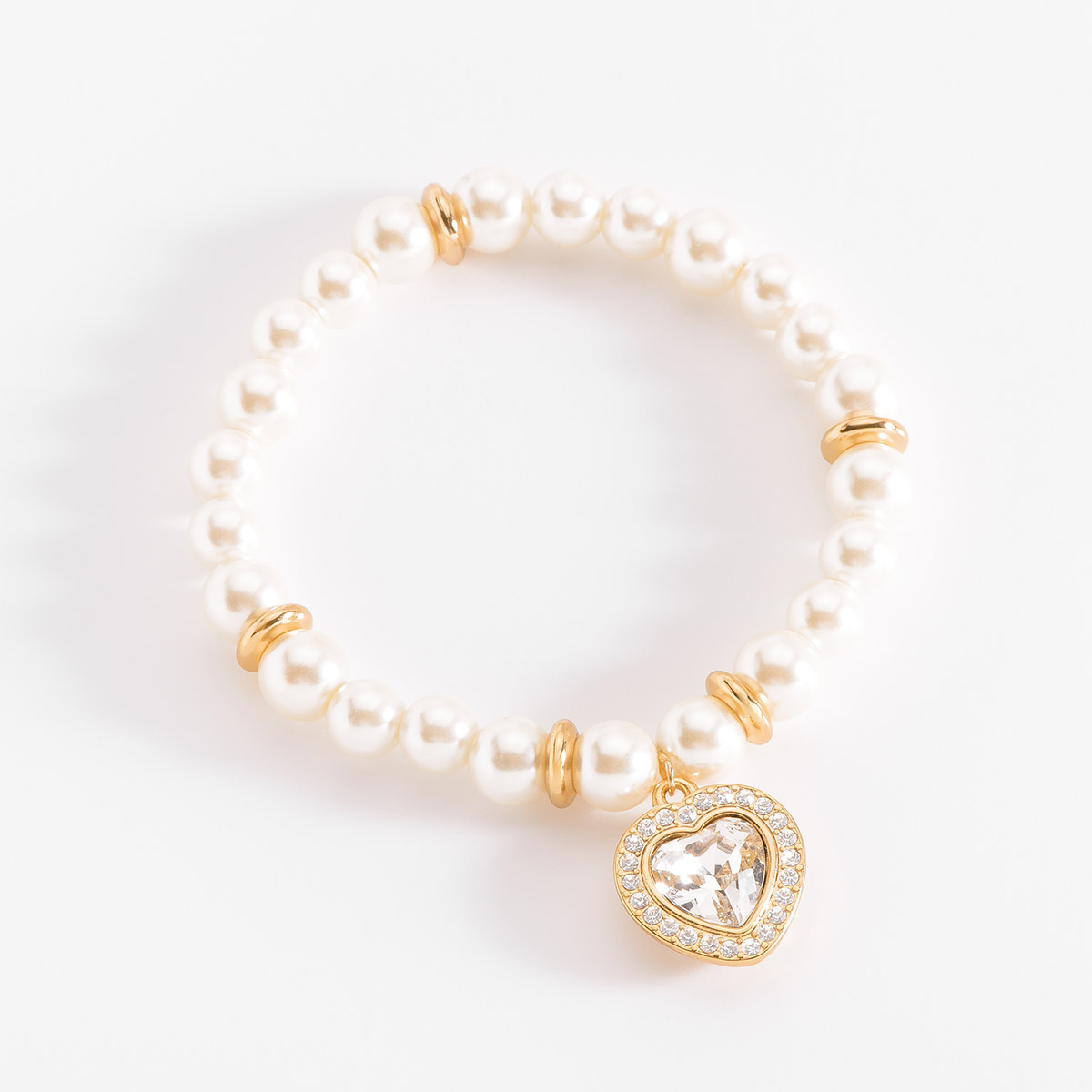 Pulsera incrustada con perlas en tono cream. Con aros en baño de oro y un dije al centro en forma de corazón. El corazón está rodeado por un halo de pequeñas piedras en tono cristal. Combínala con tu collar y aretes.
-        Pulsera
-        Medida única
-        Baño de Oro 18k
-        Perlas en tono cream
-        Piedras en tono cristal
