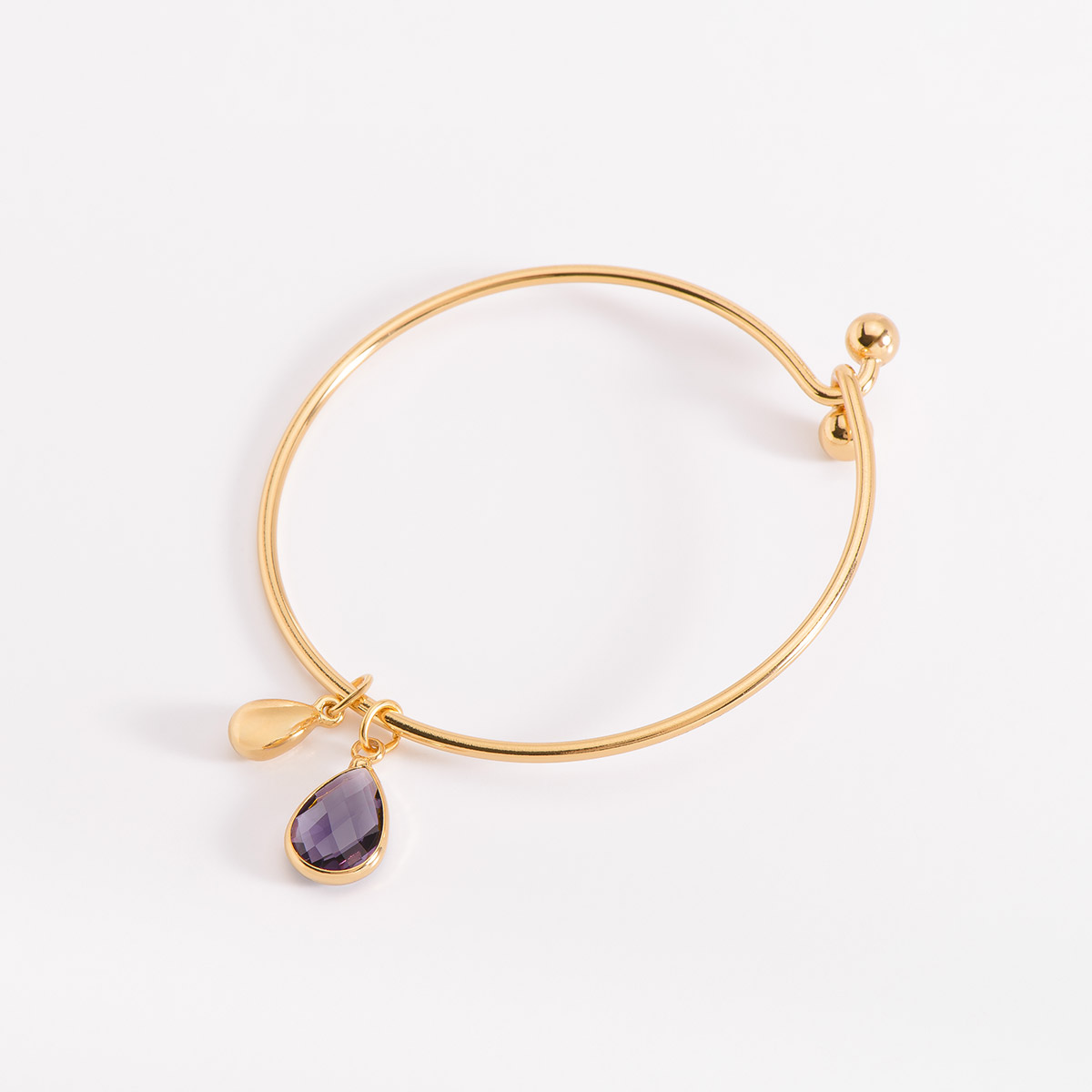 Pulsera en baño de oro, de medida única, se destaca por sus dos dijes colgantes, uno piedra en tono morado en forma de lágrima y otra lágrima más pequeña dorada.
-        Pulsera
-        Medida única
-        Baño de Oro 18k
-        Diamonice™ en tono cristal
