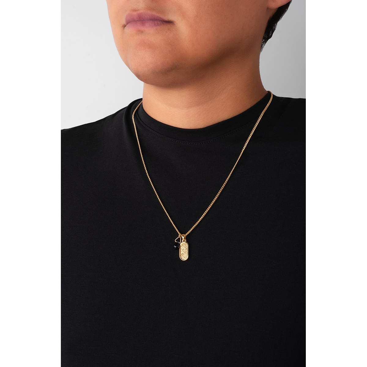 Collar en baño de oro, con dos dijes, uno ovalado y grabado con un patrón geométrico. Otro dije con una piedra en forma de lágrima, en tono azul oscuro.
-        Collar
-        55 cm
-        Baño de Oro 18k